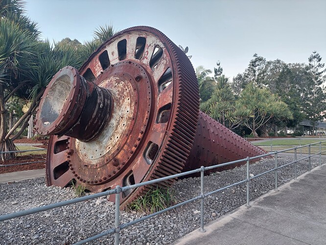 a old rusted piece of heavy machinery half buried in the ground. It looks like a large cog with a spiked cylinder on top